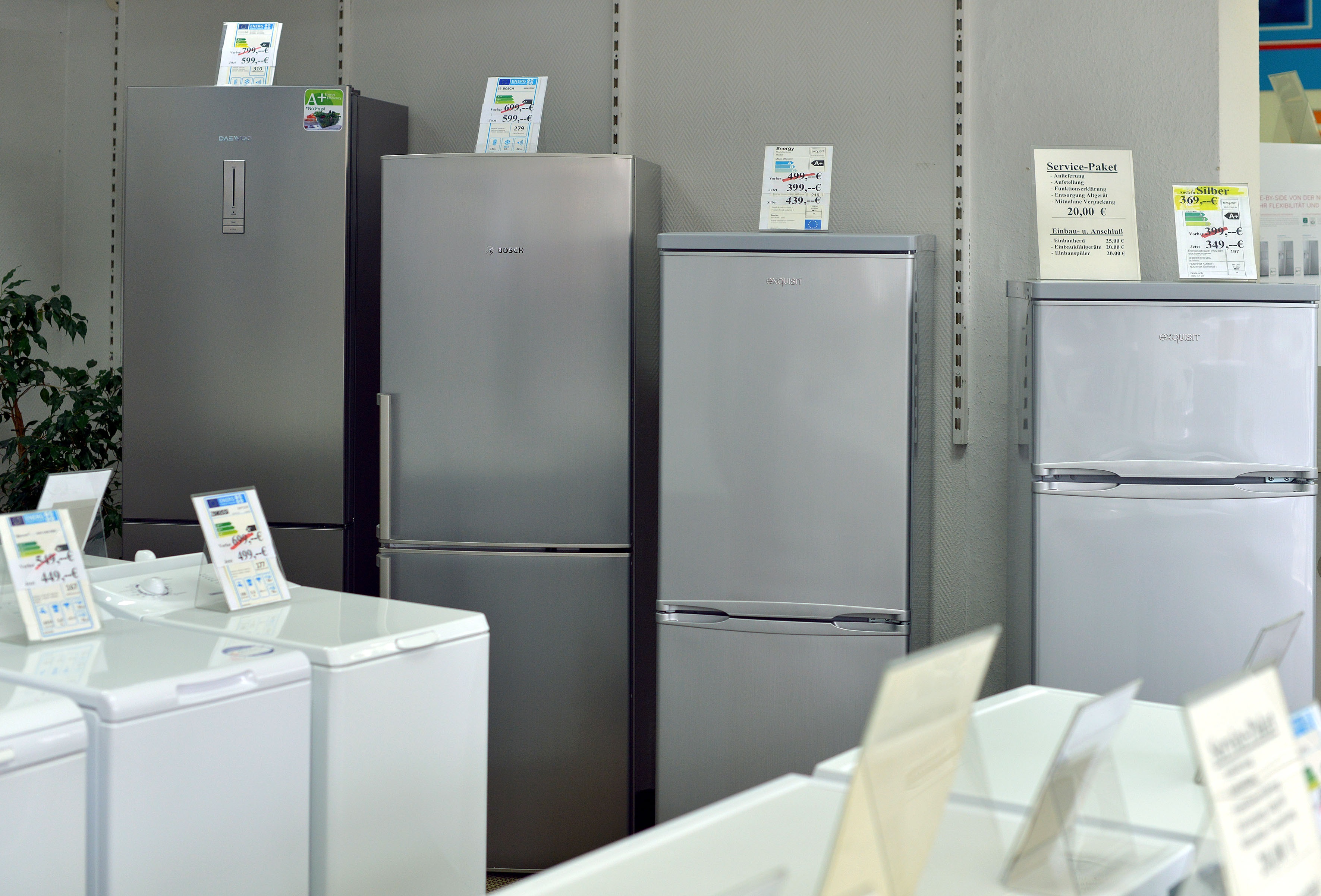 Mehrere Kühlschränke nebeneinander in einem Geschäft, Preisschilder oben drauf.