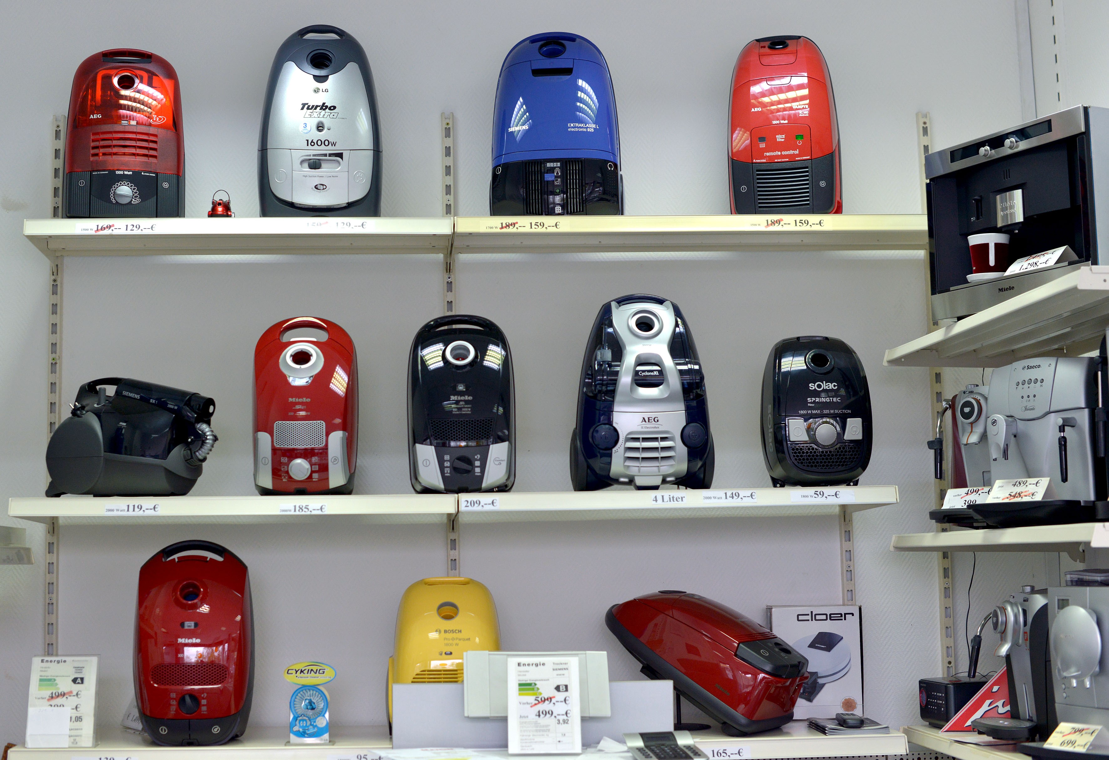 Staubsauger verschiedener Farben und Modelle auf Regalen in einem Geschäft ausgestellt.