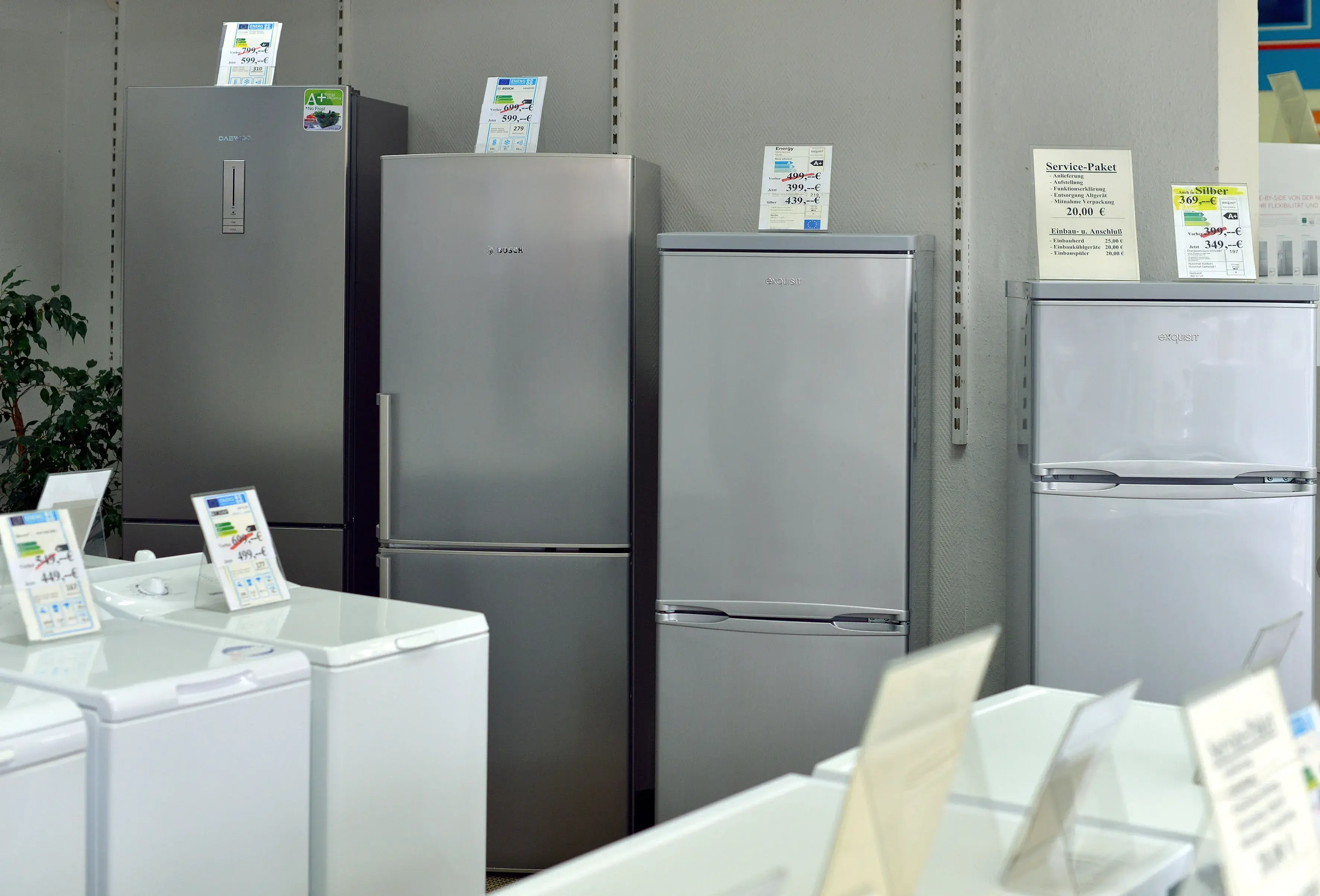 Mehrere Kühlschränke nebeneinander in einem Geschäft, Preisschilder oben drauf.