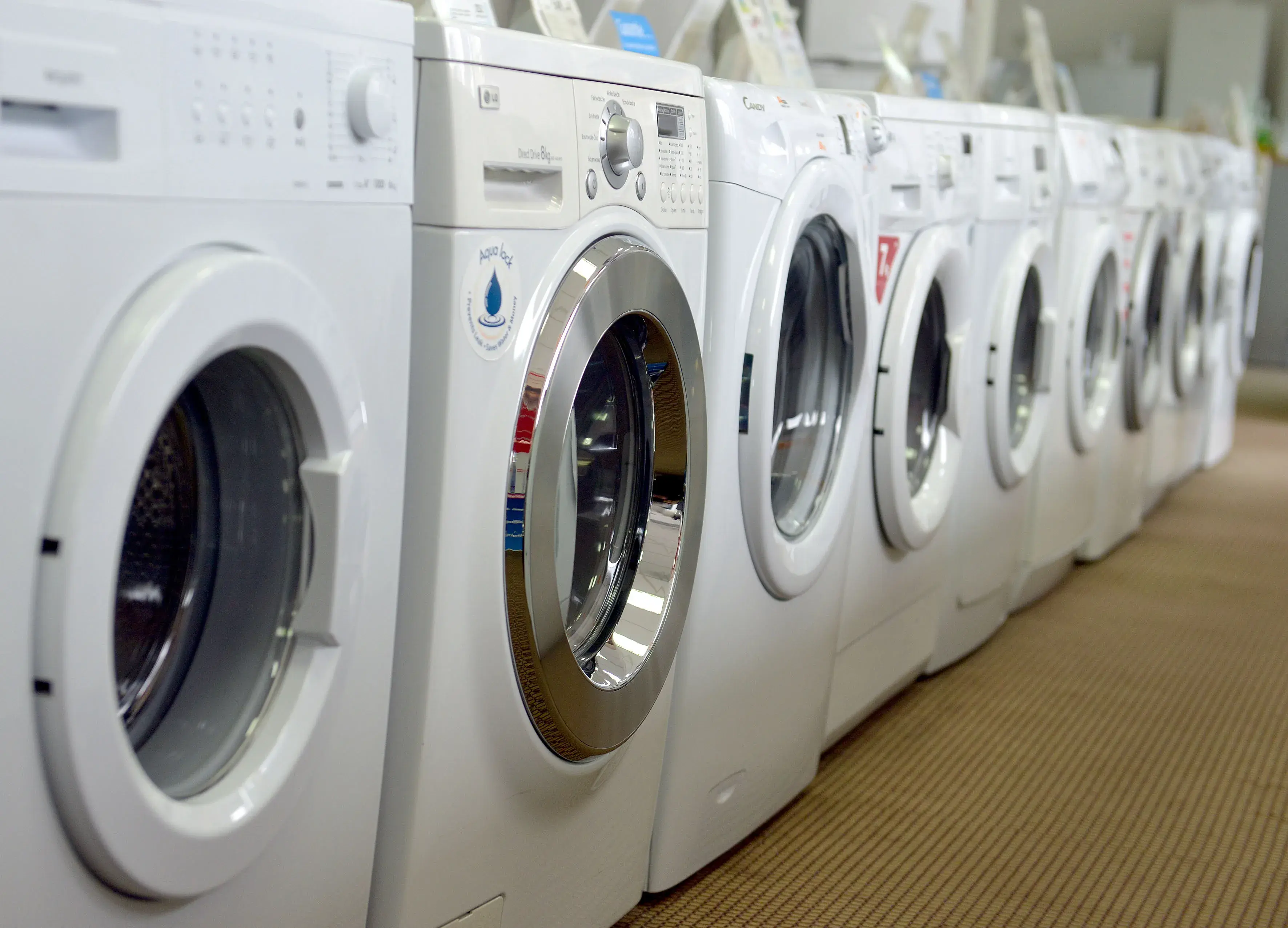 Reihe weißer Waschmaschinen auf beigem Teppich in einem Geschäft